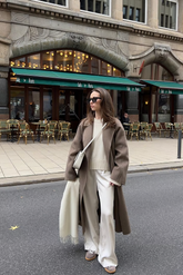 a lady in a white sweater, a brown long wool coat and a pair of white pants